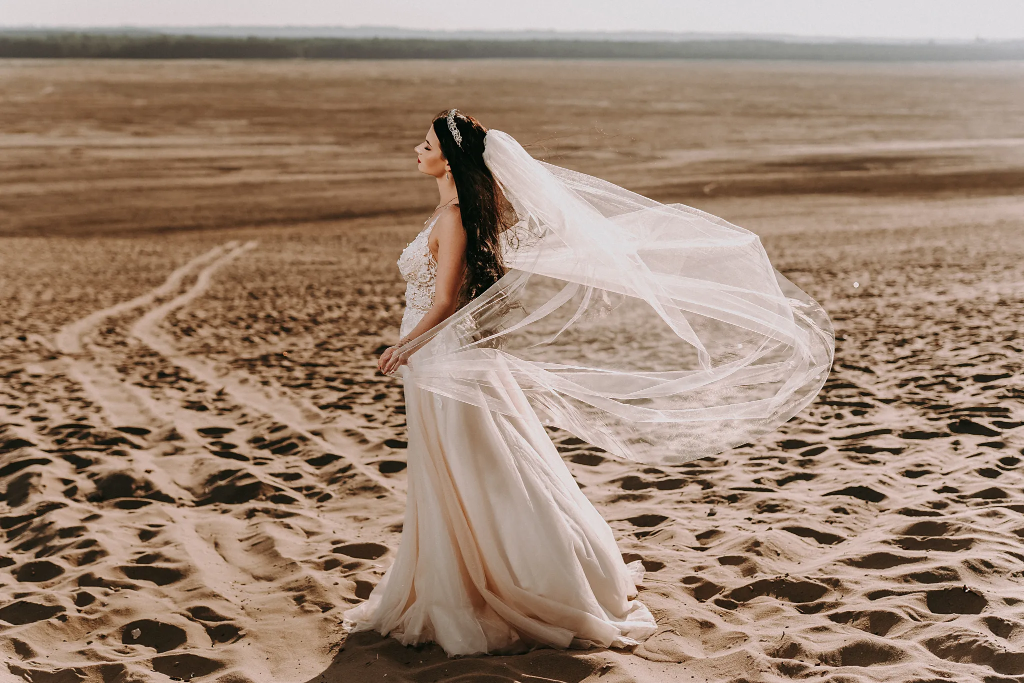 rozmazona pani mloda w niepozowanej scenie podczas sesji na pustynik z diadememn na glowie oraz pieknym dlugim welonem podazajaca w strone slonca fotograf slubny orzesze