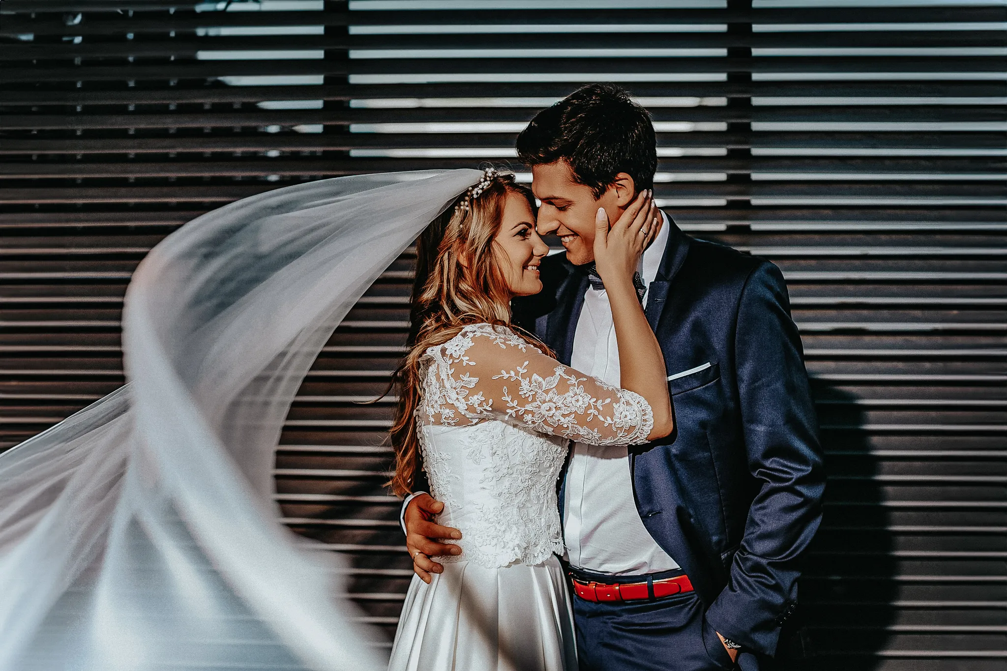 niepozowana sesja slubna mlodej pary w centrum Katowic. Para mloda zwrocona twarzami do siebie panimloda z dlubim welonem a pan mlody trzyma reke w kieszeni i posiada niebieski garnitur .okolice nospr