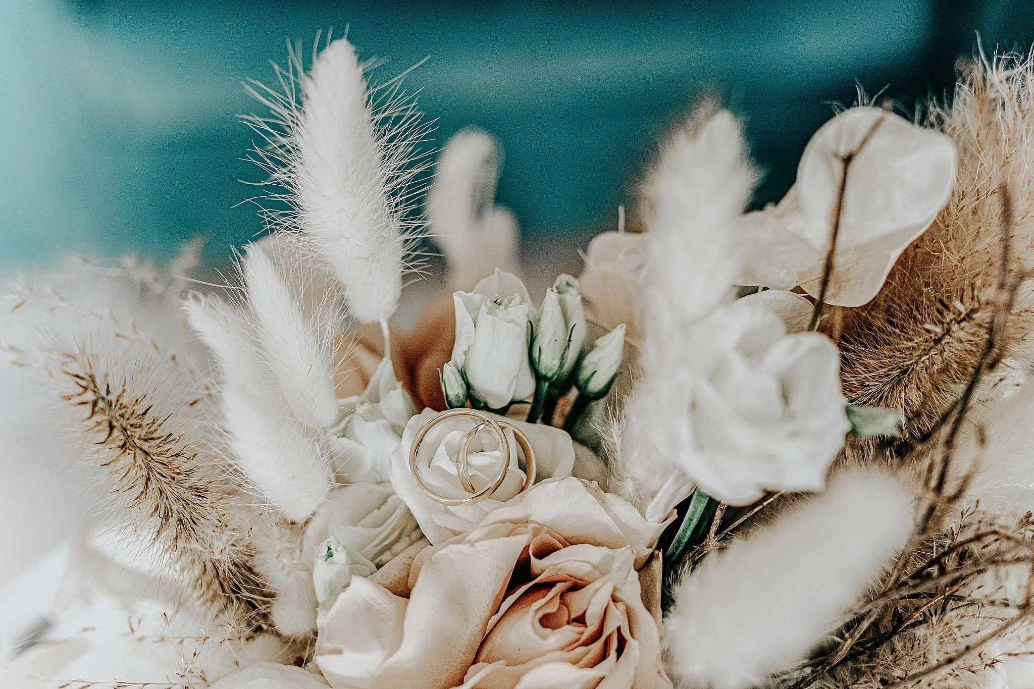 obraczki slubne jako detal pokazane na tle romatycznego bukietu kwiatow w pastelowych kolorach