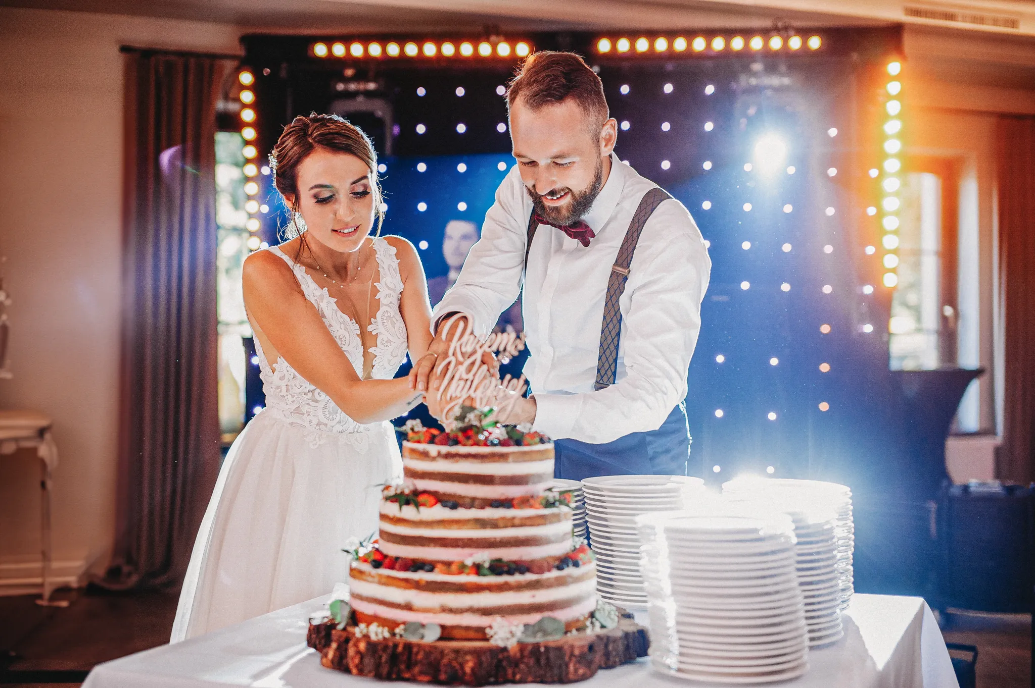 para mloda kroi pierwszy kawalek torta w klimatycznej kolorowej sali dworu modrzewiowego w gliwicach. w tle scena dj.matyjas. fotograf na slub gliwice