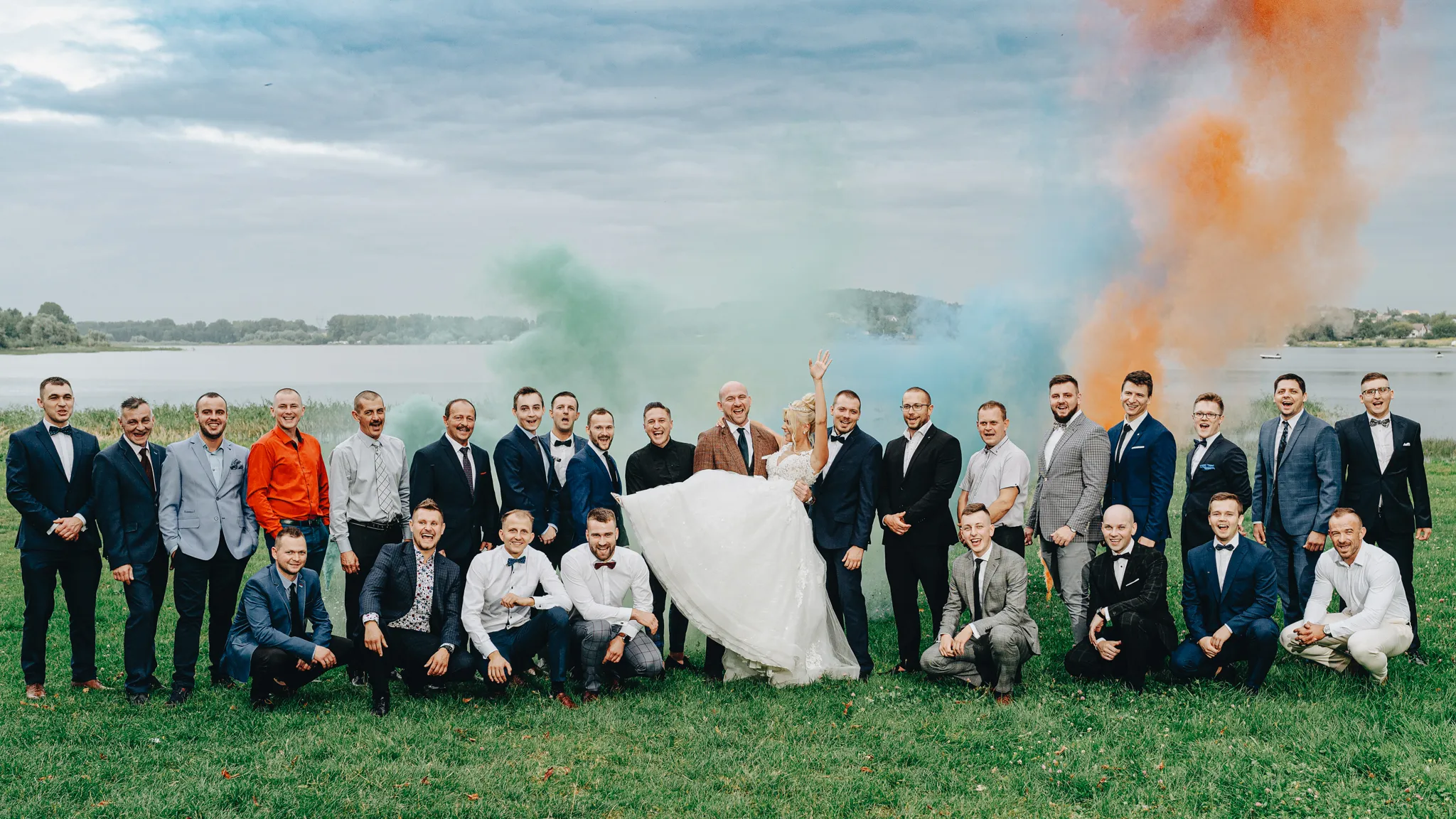 mloda pani trzymana na rekach mezczyzn podczas przyjecia weselnego w goscincu paradise w przeczycach nad brzegiem jeziora. w tle race dymne kolorowe zdjecia slubne tychy